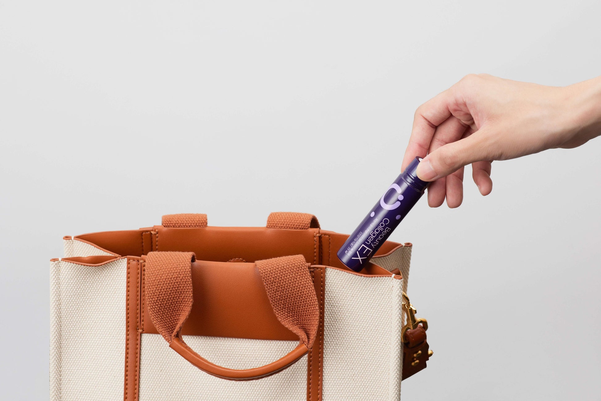 Hand placing Beauty Collagen EX into a stylish tote bag, showcasing convenience and portability.