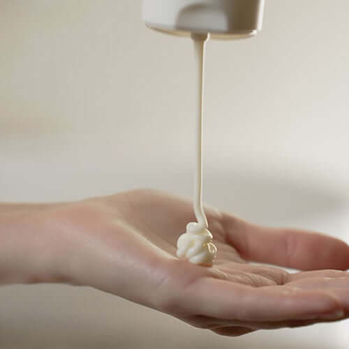 Suamela Nourishing Body Cream being dispensed onto a hand, showcasing its rich and creamy texture.