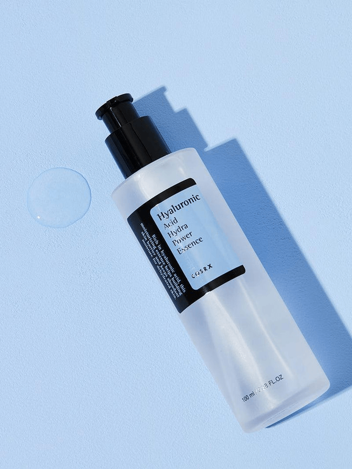 COSRX Hyaluronic Acid Hydra Power Essence bottle on a blue background, showcasing its hydrating properties.