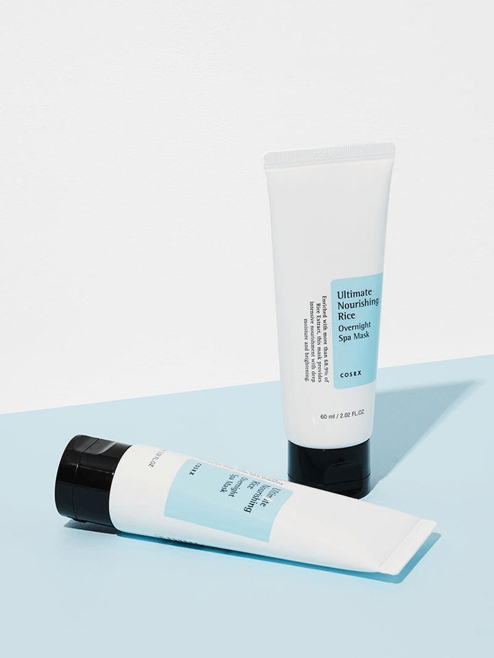 COSRX Ultimate Nourishing Rice Overnight Spa Mask tubes on a blue surface for skincare rejuvenation.