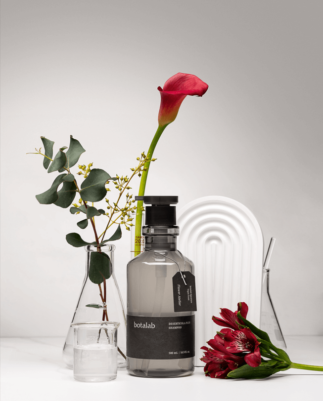 Riman Botalab Deserticola Plus Shampoo bottle displayed with flowers and greenery on a minimalistic background.