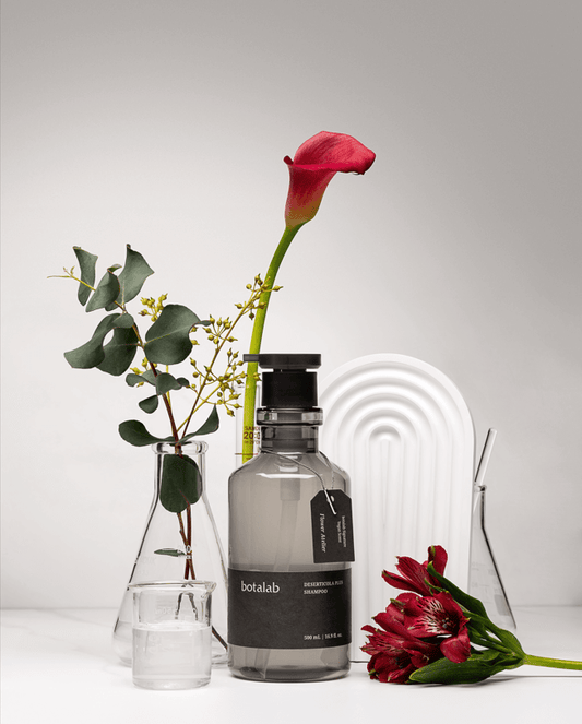 Riman Botalab Deserticola Plus Shampoo bottle displayed with flowers and greenery on a minimalistic background.