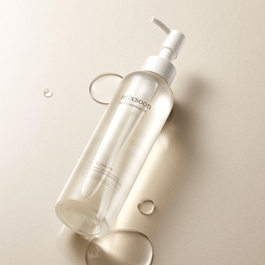 mixsoon Bean Cleansing Oil in a clear bottle on a beige background with droplets of cleansing oil.