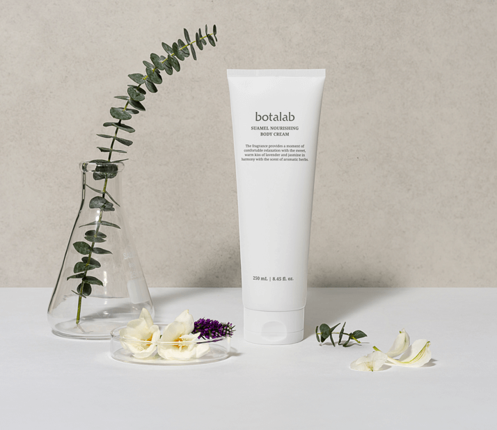 Suamela Nourishing Body Cream tube beside flowers and eucalyptus, showcasing fast-absorbing hydration and soothing ingredients.