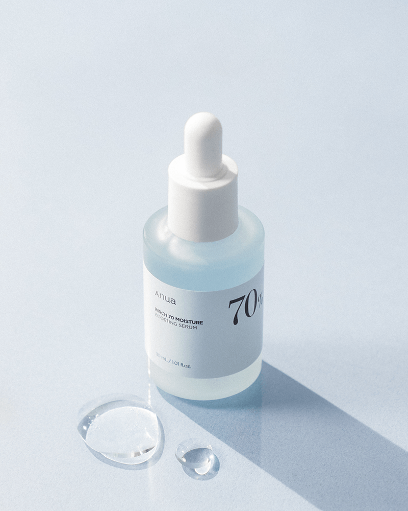 Anua Birch 70 Moisture Boosting Serum in a glass dropper bottle with serum droplets on blue background.