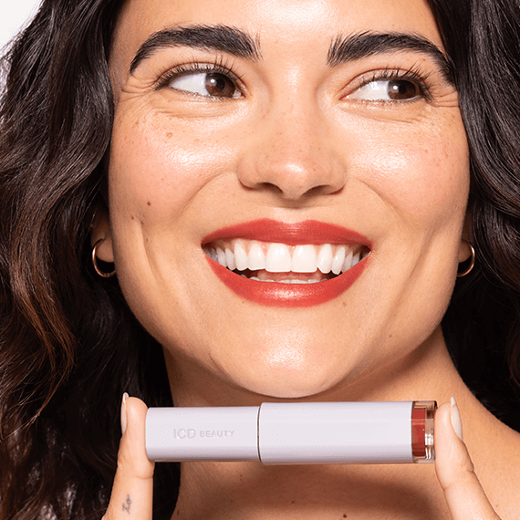 A smiling woman holds ICD Makeup Butter Lip Tint Semi Matte, showcasing its rich color and shine.