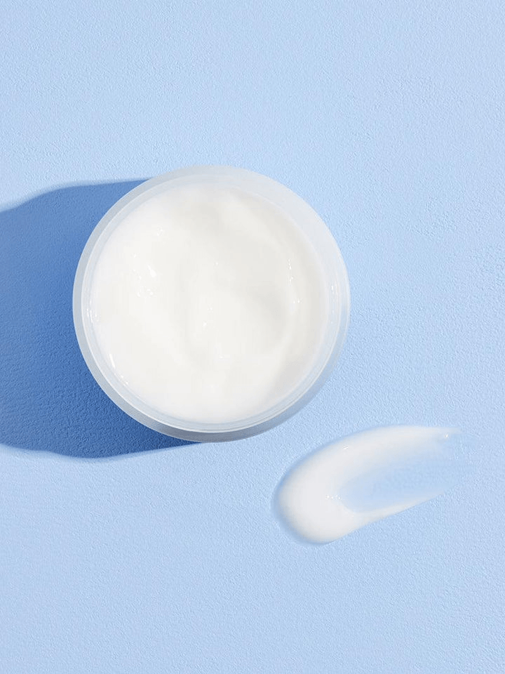 COSRX Hyaluronic Acid Intensive Cream in a clear jar with a dollop of cream beside it on a blue background.