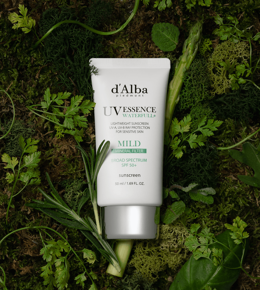 d'Alba White Truffle Waterfull Mild Sunscreen SPF 50 on a bed of green leaves, showcasing its lightweight formulation.