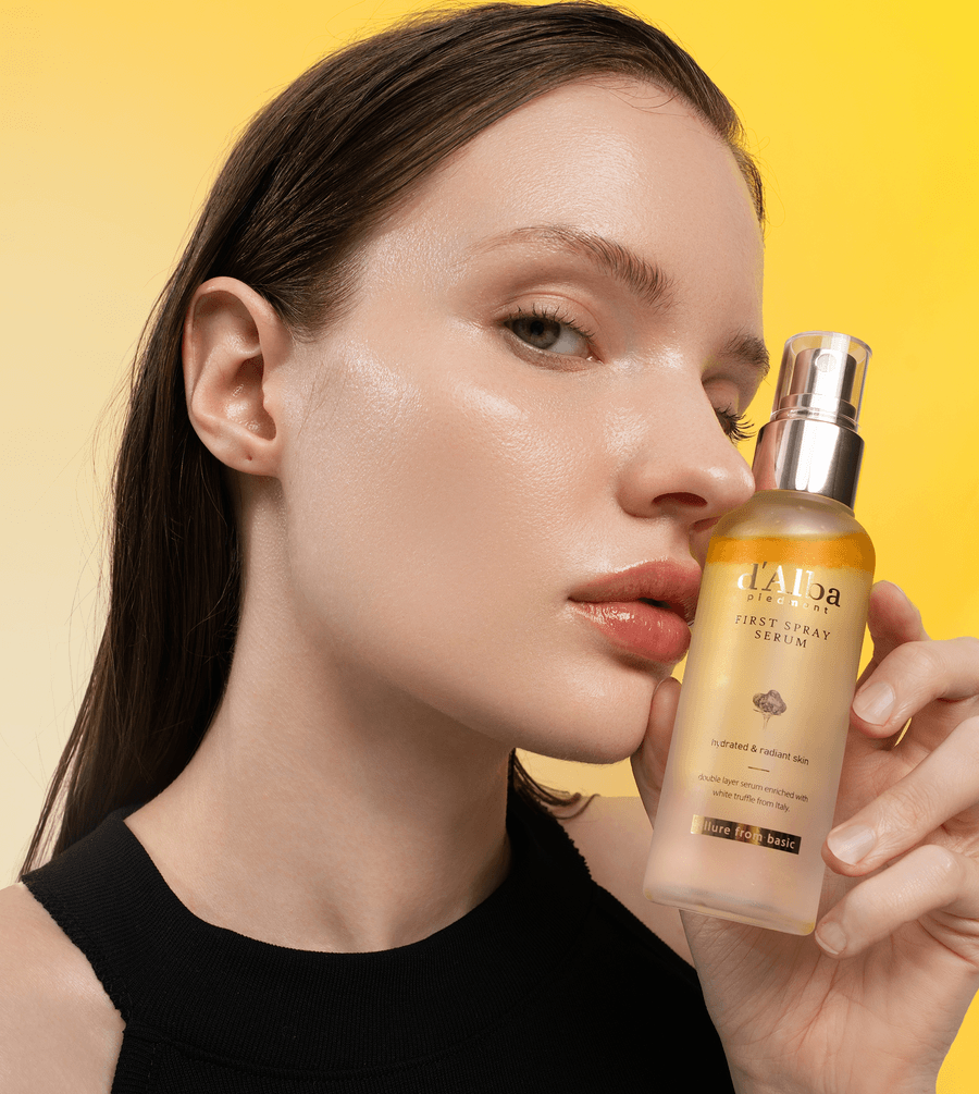 d'Alba White Truffle First Spray Serum held by a model with glowing skin against a yellow background