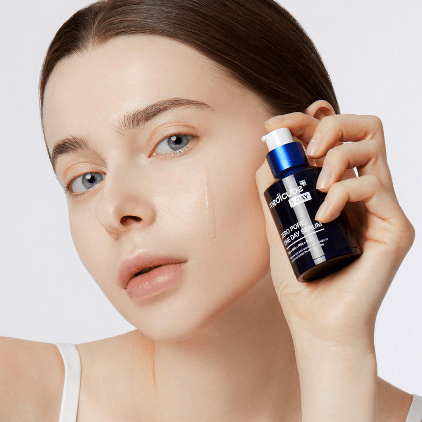 Person holding Medicube Zero Pore One-day Serum, showcasing the bottle with clear skin and visible serum on fingers.