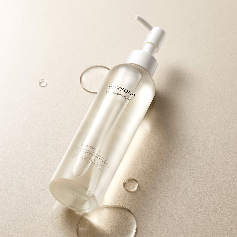 mixsoon Bean Cleansing Oil in a clear bottle on a beige background with droplets of cleansing oil.