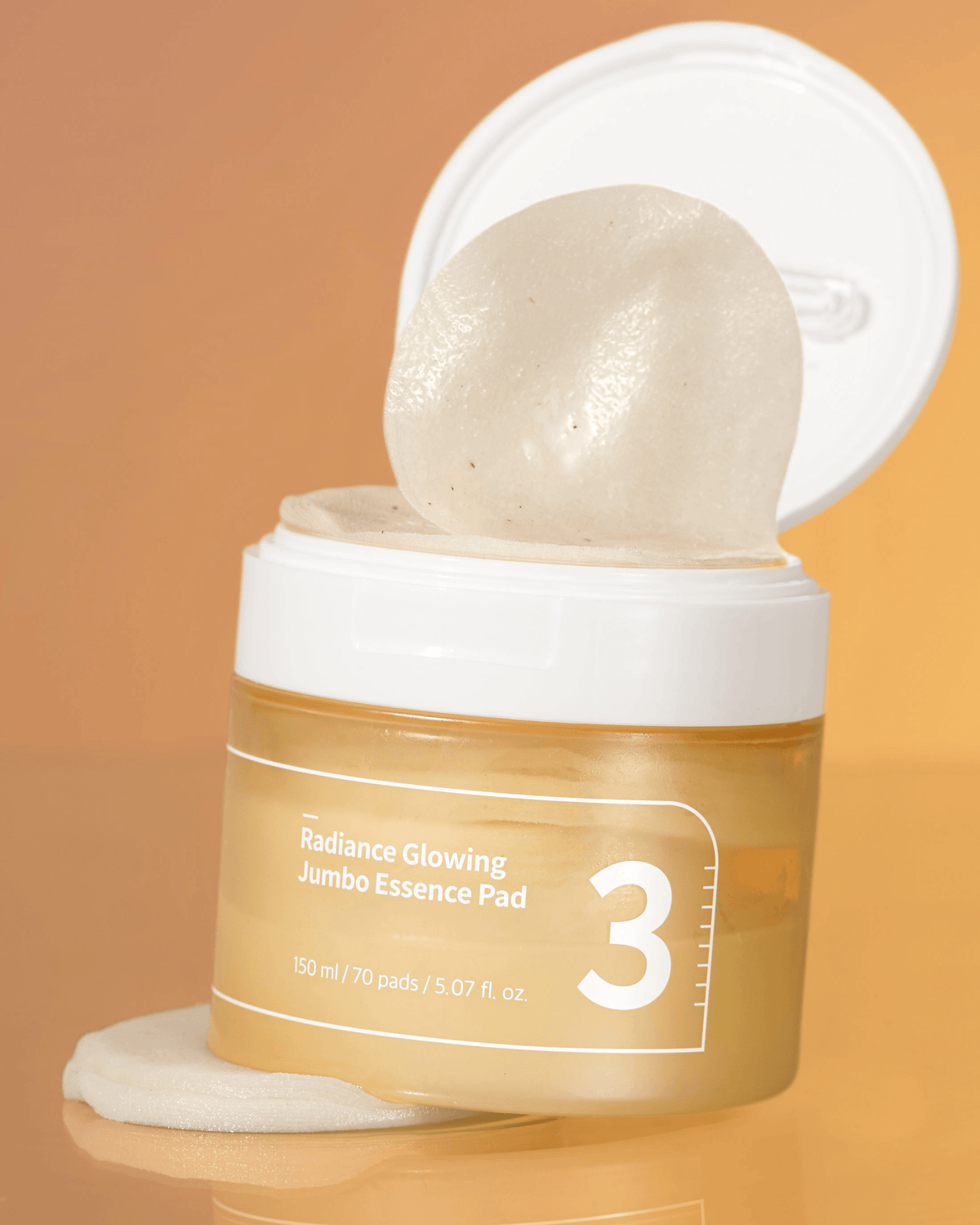 numbuzin No.3 Radiance Glowing Jumbo Essence Pads in a jar with a pad lifted, showcasing its essence-rich formula.