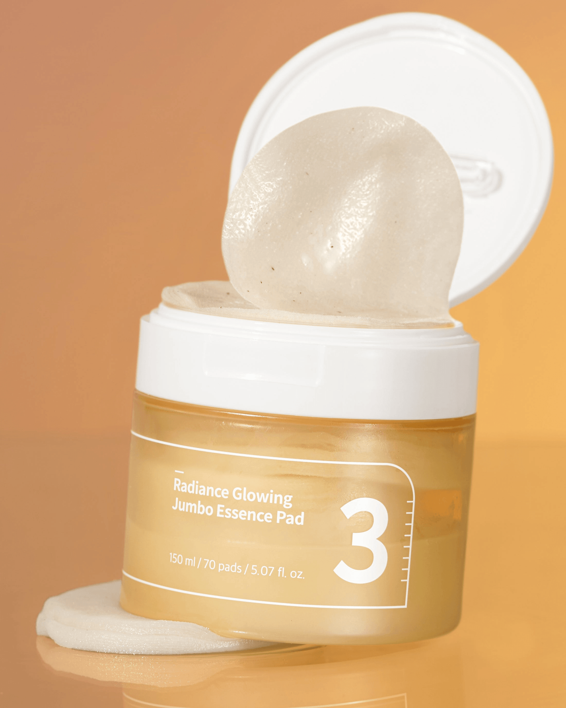 numbuzin No.3 Radiance Glowing Jumbo Essence Pads in a jar with a pad lifted, showcasing its essence-rich formula.